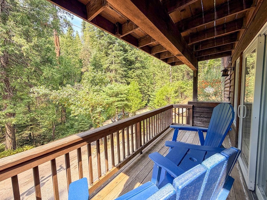 Covered balcony with Adirondack chairs overlooking the forest at Boom Chalet